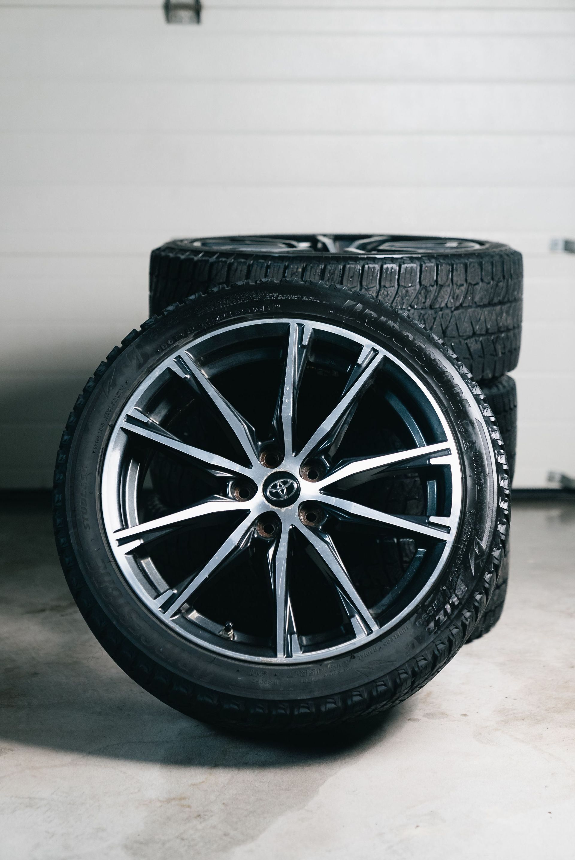 Close-up of stacked car tires and alloy wheels in a garage setting, showcasing automotive equipment.