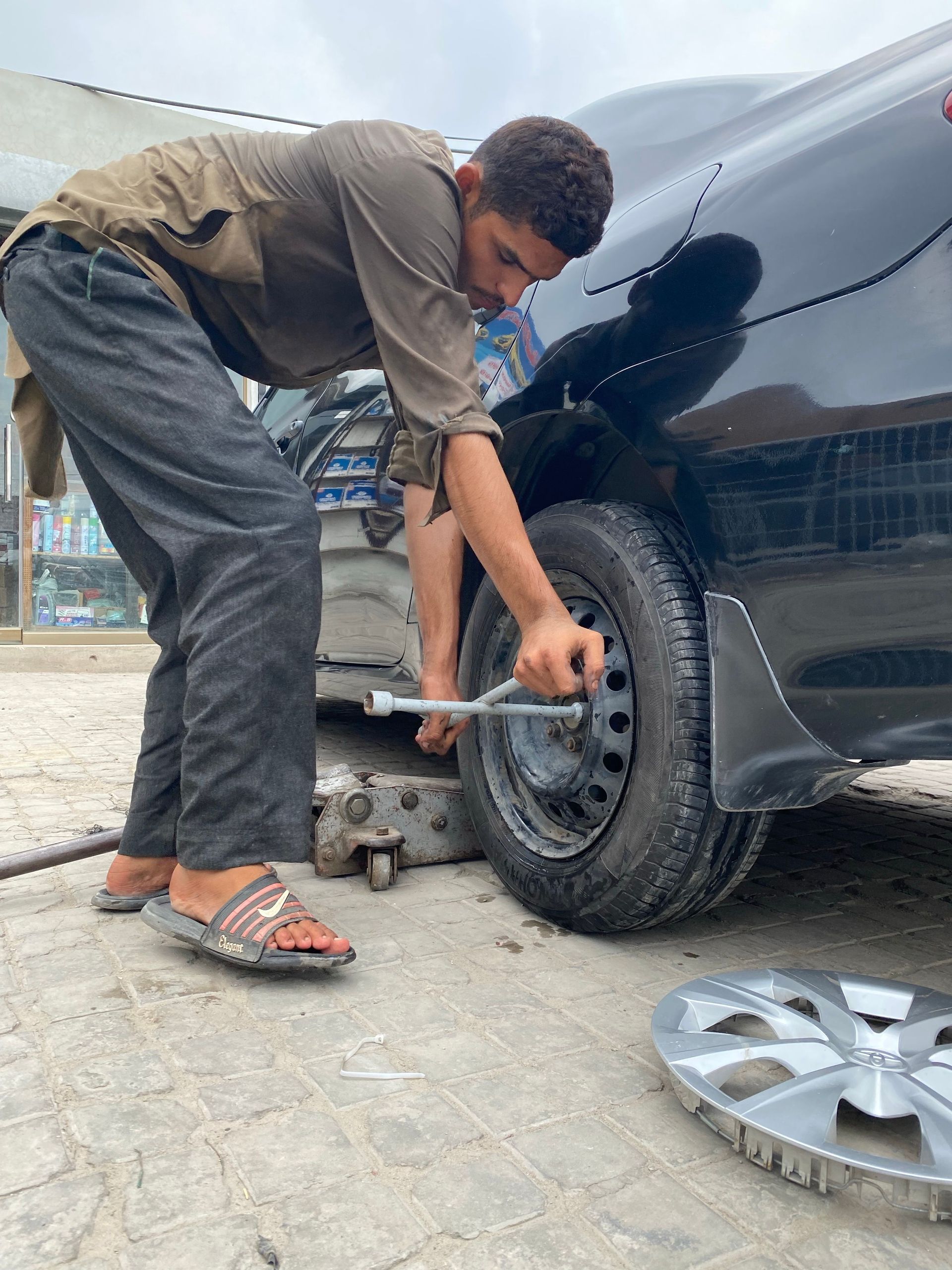 A young mechanic uses a lug wrench to fix a car tire outdoors.
