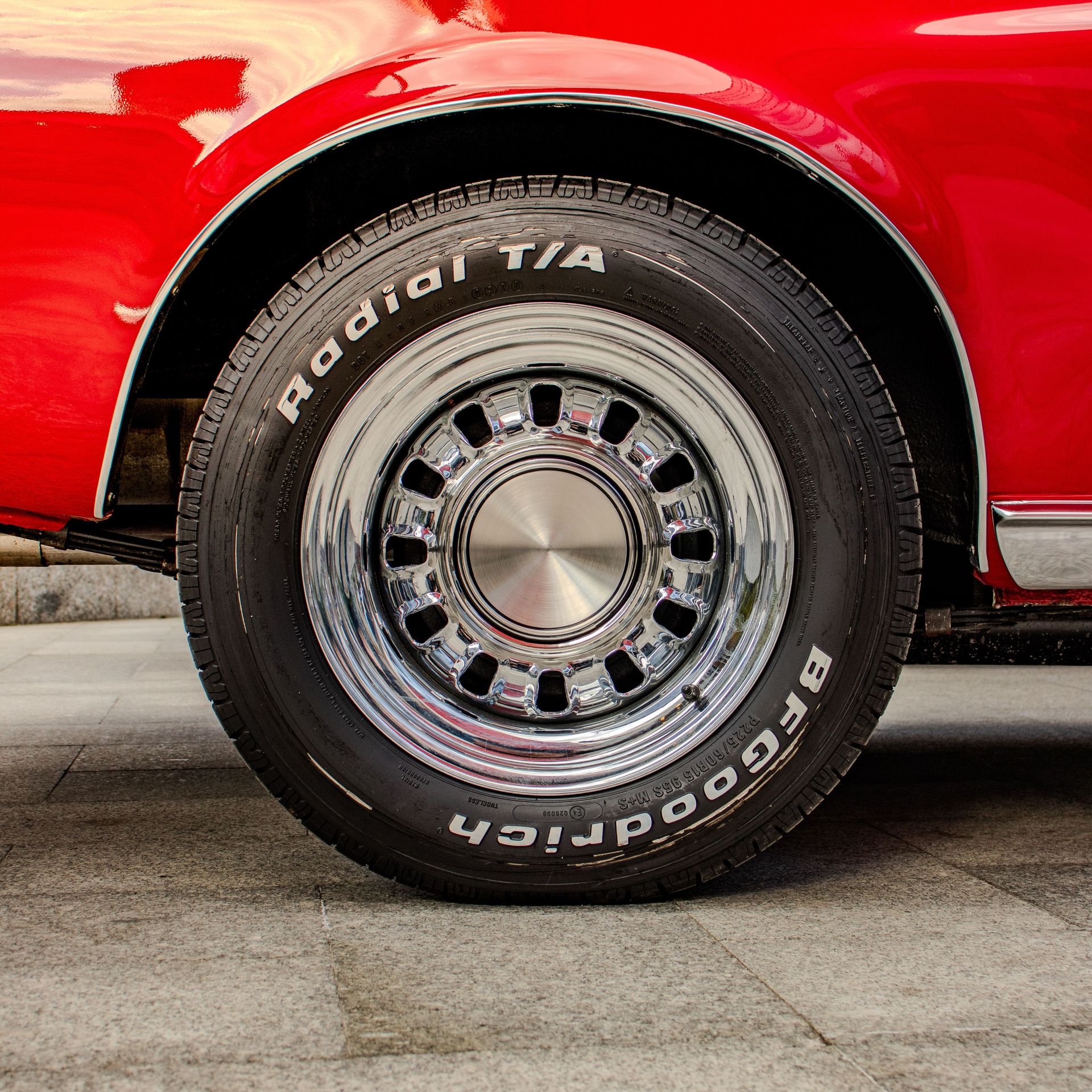 Detailed shot of a vintage car's tire and chrome rim reflecting its classic appeal.